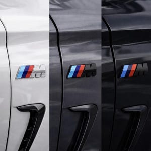 Pode incluir: Close-up de três painéis de portas de carro, cada um com um emblema BMW M de cor diferente. Os emblemas apresentam detalhes azuis, vermelhos e prateados ou pretos. As portas dos carros são brancas, cinzentas e pretas.