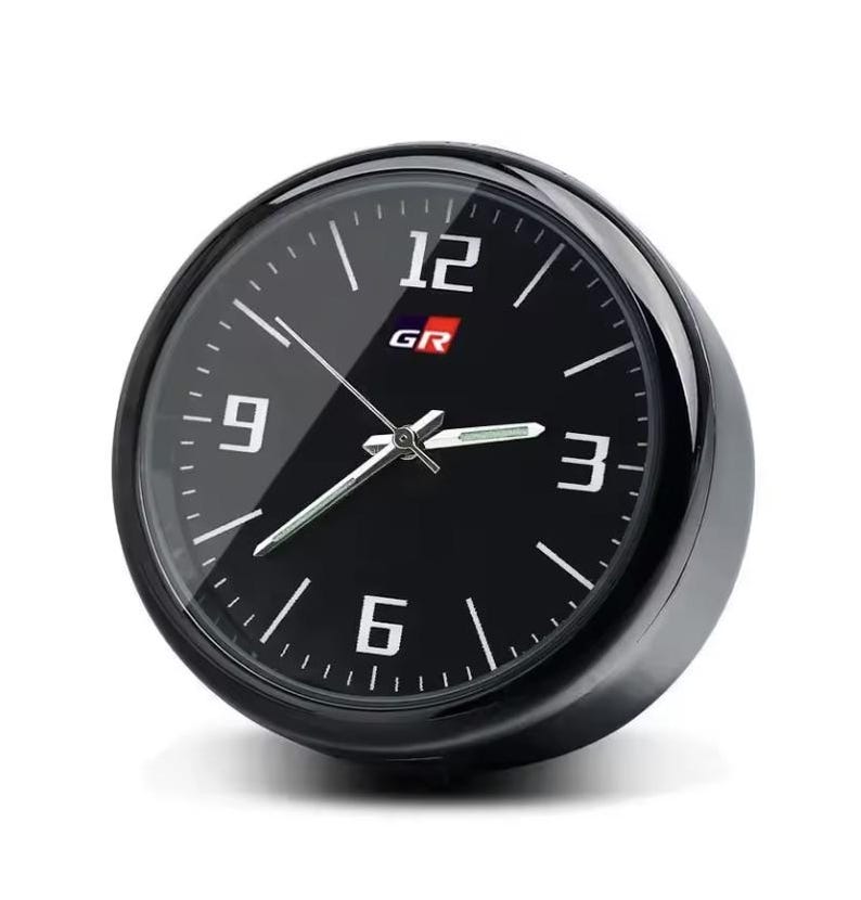 K&ouml;nnte beinhalten: Eine schwarze analoge Uhr mit wei&szlig;en Ziffern bei 3, 6, 9 und 12. Das Zifferblatt hat die Buchstaben "GR" in Rot und Wei&szlig;. Die Uhr hat eine schwarze L&uuml;nette und eine transparente Glasabdeckung.