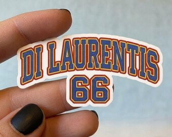 Puede incluir: Una pegatina troquelada que presenta el texto DI LAURENTIS en una fuente azul de estilo universitario con un borde rojo, situada sobre el número 66 con el mismo esquema de colores azul y rojo, sobre un fondo blanco.