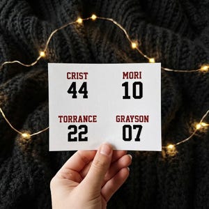 May include: A white rectangular sheet featuring four sets of names and numbers in a sports-style font. The text includes CRIST 44, MORI 10, TORRANCE 22, and GRAYSON 07. The names are printed in dark red, while the numbers are printed in black.