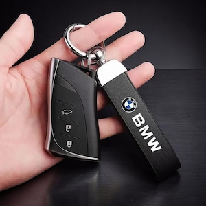 May include: Black car key and key fob with a silver key ring. The key fob has the BMW logo and the word "BMW" in white. The car key is black with silver trim and has three buttons.