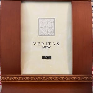 May include: A dark brown wooden picture frame with decorative detailing. The frame holds a cream-coloured mount with the word "VERITAS" and a floral design. The frame is sized for a 12.7 x 17.8cm photo.