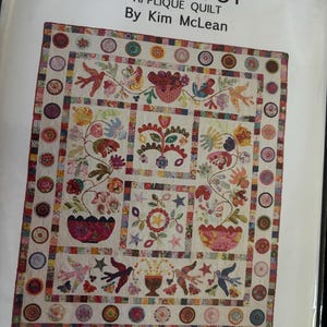 May include: A colorful applique quilt titled "Flower Pot" by Kim McLean. The quilt features floral and bird motifs in various colors, with a central flower pot design and decorative border. The quilt is displayed on a white background.