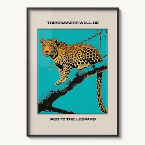 May include: A framed art print featuring a leopard perched on a tree branch against a teal background. The text "TRESSPASSERS WILL BE" is at the top, and "FED TO THE LEOPARD" is at the bottom. The leopard has a yellow and black spotted pattern.