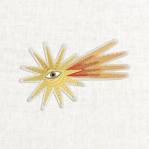 May include: Embroidered patch featuring a stylized sun with an eye at its center. The sun has gold and silver rays, with a red and orange comet-like tail extending to the right. The patch is on a white fabric background.