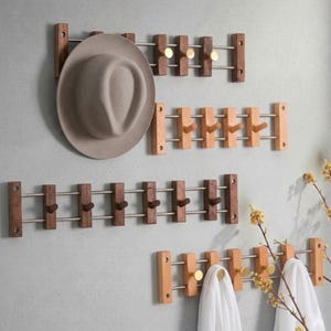 May include: Four wall-mounted racks featuring horizontal metal rods and vertical wooden slats. The racks include small pegs for hanging items. One rack holds a wide-brimmed beige hat, while another holds two white fabric cloths draped over the pegs.