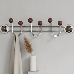 May include: A modern coat rack with six hooks. The rack features a polished chrome finish with dark brown wooden ball accents. A beige towel hangs from one of the hooks. A white vase with dried grass sits below the rack.