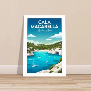 May include: A framed print featuring a scenic view of Cala Macarella in Menorca, Spain. The artwork depicts a turquoise bay with sailboats, white cliffs, and lush green trees under a bright blue sky. Text at the top reads "CALA MACARELLA Menorca, Spain."