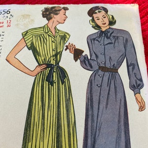 Peut inclure: Illustration vintage de patron de couture représentant deux femmes portant des robes. La femme de gauche porte une robe à rayures jaunes et blanches avec une ceinture et un nœud noirs. La femme de droite porte une robe bleue unie avec un col blanc et une ceinture marron. Le numéro du patron est 556, taille 12, tour de poitrine 30.