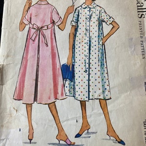 May include: Vintage McCall's sewing pattern for a dress with a button-up front and a tie at the back. The pattern is printed on white paper with a blue and white polka dot design. The pattern is labeled "Easy to Sew" and "Printed Pattern".