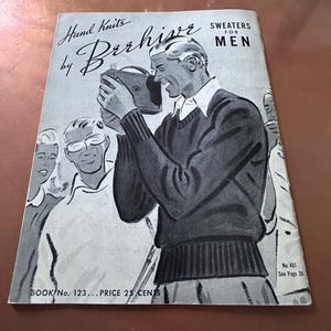 Op de afbeelding: Een zwart-witte illustratie van een man die een trui draagt en een camera vasthoudt. De afbeelding is afkomstig uit een vintage breipatronenboek voor truien. De tekst op de omslag van het boek luidt "Hand Knits by Beehive Sweaters for Men, Book No. 123, Price 25 Cents, No. 461, See Page 30."