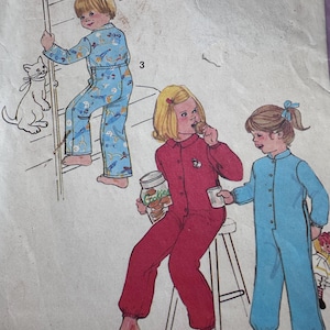 Può includere: Un modello di cucito vintage con tre bambini che indossano pigiami. Il modello include istruzioni per realizzare un set di pigiama blu e bianco, un set di pigiama rosso e un set di pigiama blu. Il modello è etichettato con i numeri 2 e 3.