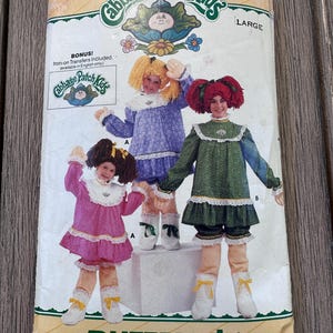 Puede incluir: Un patrón de costura Butterick vintage con disfraces de Cabbage Patch Kids. El patrón muestra a tres niños con trajes de muñeca con pelucas y botas a juego. El patrón está etiquetado como "Large" e incluye transferencias termoadhesivas.