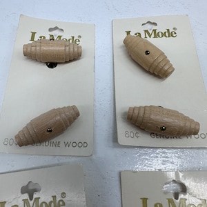 May include: Four packages of wooden toggle buttons labeled "La Mode" with the price of 80 cents. The buttons are made of genuine wood and are a light brown color.