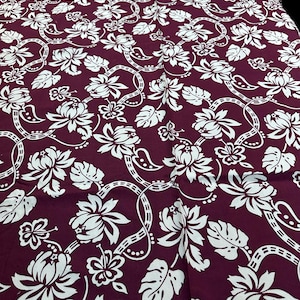 Könnte beinhalten: Burgunderfarbener Stoff mit einem sich wiederholenden Muster aus weißen floralen Designs und miteinander verbundenen Ranken. Die Blumen sind stilisiert mit mehreren Blütenblättern und Blättern, wodurch ein tropisches oder botanisches Thema entsteht.