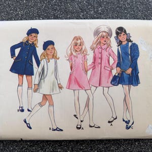 May include: A Butterick 5626 sewing pattern envelope for girls' sizes 7, 8, 10, 12, and 14. The front features illustrations of five figures wearing various coats and dresses in blue, white, and pink, paired with hats, tights, and shoes.