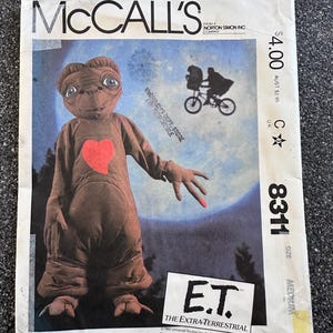 May include: Vintage McCall's sewing pattern featuring E.T. the Extra-Terrestrial. The pattern cover shows E.T. with a red heart and a silhouette of E.T. on a bicycle. The pattern is size medium, with the number 8311.