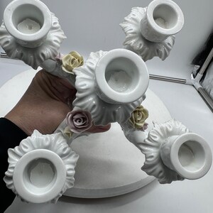 May include: White porcelain candelabra with five candle holders and floral accents. The candelabra is decorated with delicate white roses and leaves.