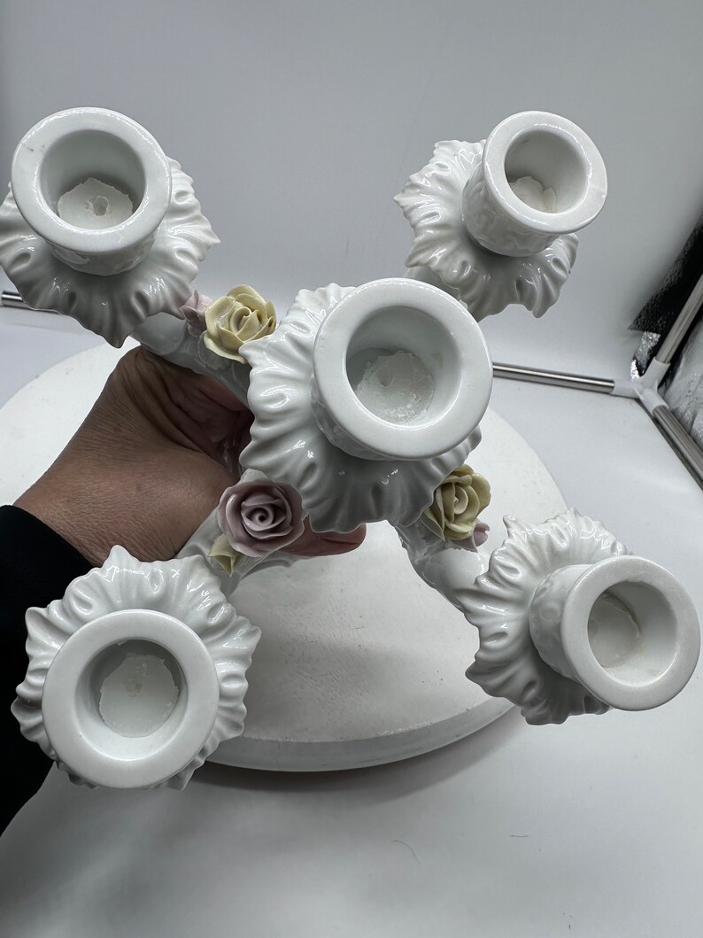 May include: White porcelain candelabra with five candle holders and floral accents. The candelabra is decorated with delicate white roses and leaves.