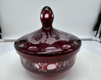 Puede incluir: Un plat de dulces de vidrio rojo rubí vintage con tapa. El plato está decorado con un diseño floral grabado y detalles en vidrio transparente.