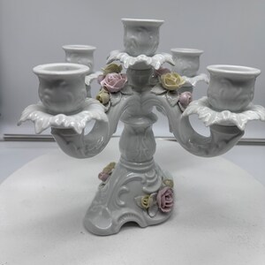 May include: White porcelain candelabra with five candle holders and floral accents. The candelabra is decorated with delicate pink and yellow roses.