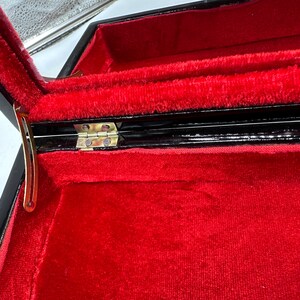 Puede incluir: Una caja de madera negra con un interior de terciopelo rojo y una bisagra dorada. La caja est&aacute; abierta y el interior es visible.