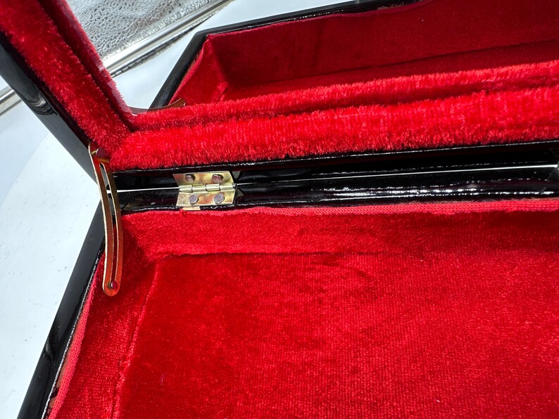 Puede incluir: Una caja de madera negra con un interior de terciopelo rojo y una bisagra dorada. La caja est&aacute; abierta y el interior es visible.