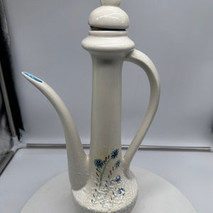 May include: White ceramic teapot with a floral design and a lid. The teapot has a textured surface and a spout.