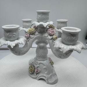May include: A white porcelain five-arm candelabra with floral accents. Each arm features a delicate rose and leaf design. The base is intricately detailed with a floral motif.