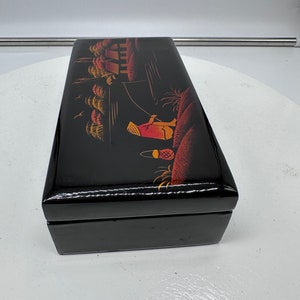 Puede incluir: Caja de madera negra con una escena pintada a mano de una persona con un sombrero y ropa tradicionales pescando en un r&iacute;o con casas y &aacute;rboles en el fondo.