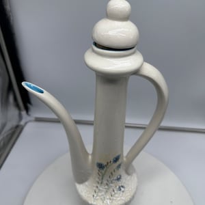 May include: White ceramic teapot with a blue floral design and a white lid. The teapot has a spout and a handle.