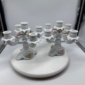 May include: A pair of white porcelain candle holders with floral accents. Each holder has five candle cups and features delicate pink and yellow roses.