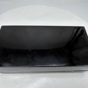 Puede incluir: Una caja rectangular negra con un acabado brillante. La caja est&aacute; cerrada y tiene una superficie lisa.