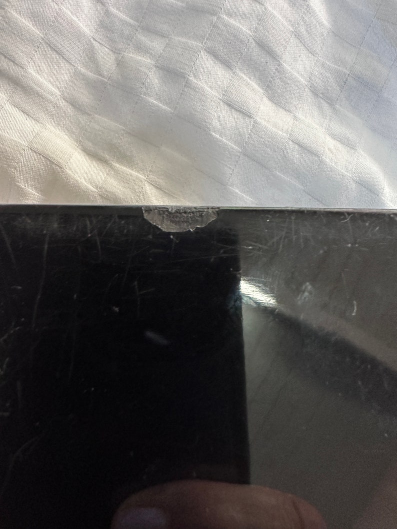 Puede incluir: Una superficie de vidrio negro con un peque&ntilde;o astillado en el borde superior. La superficie est&aacute; rayada y muestra signos de desgaste.