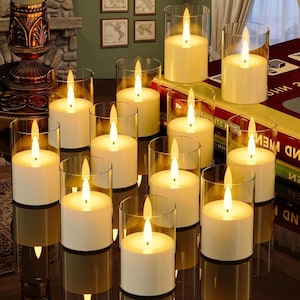 Könnte beinhalten: Eine Ansammlung weißer Kerzen in transparenten Glashaltern. Die Kerzen haben einen warmen, leuchtenden Flammeneffekt. Die Kerzen sind auf einer reflektierenden Oberfläche angeordnet. Heimdekoration.