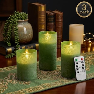 Op de afbeelding: Drie groene LED-pijlerkaarsen met een getextureerde afwerking en een afstandsbediening. De kaarsen zijn gerangschikt op een groene loper met gouden rand. Een "3-pack" sticker staat rechtsboven.