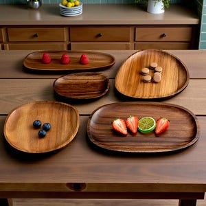 May include: A collection of wooden serving platters in various shapes, including oval and irregular forms. The platters are filled with fresh fruit and pastries, such as strawberries, blueberries, and macarons. The wood grain is visible, showcasing a natural, warm tone.