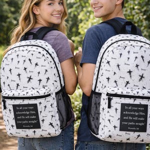 May include: Two white backpacks with a black cross and "Jesus" pattern. Each backpack has a black mesh side pocket and a black rectangular patch with text. The backpacks are worn by two people.