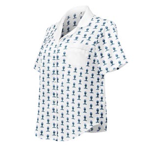 May include: White short-sleeved button-down shirt with a repeating pattern of blue alien head figures. The shirt has a white collar and a chest pocket. The fabric appears to be lightweight.