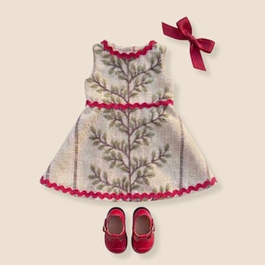 May include: A sleeveless dress featuring a beige fabric with a vertical green leaf pattern, accented by red rickrack trim at the neckline, waist, and hem. The set includes a matching red fabric hair bow and a pair of red T-strap shoes.