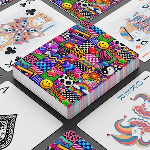 Op de afbeelding: Een pak speelkaarten met een kleurrijk, patroonontwerp op de achterkant. Het pak bevat verschillende symbolen, waaronder smileygezichten, sterren, harten en regenbogen. Individuele kaarten zijn zichtbaar, waaronder de schoppenaas, klaverkoning en joker.