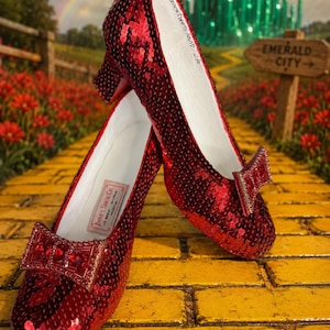 Puede incluir: Un par de zapatos de tacón rojos con lentejuelas, tacón bajo y un lazo decorativo en la punta. El interior del zapato muestra un forro blanco con el texto Innes Shoe Co. y la firma #7 Judy Garland escrita en el lado interior.