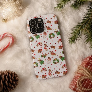 May include: A white smartphone case featuring a repeating pattern of brown dachshunds wearing holiday sweaters and reindeer antlers, interspersed with green wreaths, Christmas trees, and small red polka dots across the entire surface.