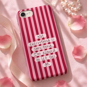 May include: A pink and red striped phone case with the text "Not everything is something. I'm allowed to let this go." The case is surrounded by pink rose petals and a pearl necklace.