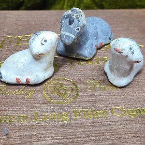 May include: Three small, hand-painted animal figurines in a seated position. Two figurines are white with subtle grey and orange accents, while the central figurine is grey with black markings. Each piece features a smooth, matte texture and simple details.
