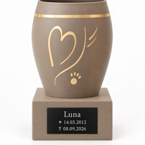 Op de afbeelding: Een walnootbeige urn met een goudkleurige band, een gouden hartomtrek en een pootafdruk. De urn staat op een vierkante voet met een zwart plaatje met de tekst: Luna, * 14.03.2012, † 08.09.2026. Het woord Walnussbeige staat eronder gedrukt.