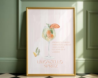 May include: A framed watercolor print featuring a Limoncello Spritz cocktail. The drink is in a stemmed glass, garnished with orange slices and rosemary. Text on the print lists ingredients. The frame is gold.