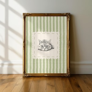 Può includere: Una stampa incorniciata con una dettagliata illustrazione in bianco e nero del volto di un gatto. L'opera d'arte è ambientata su uno sfondo di strisce verticali verdi e bianche, incorniciata in una cornice dorata ornata. La stampa è esposta su un pavimento in legno.