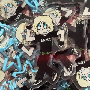 May include: Clear acrylic keychain featuring a cartoon character with blonde hair and blue eyes, wearing a black shirt with "ARMY" printed on it. The character is in a dynamic pose, with a number 1. The keychain has a blue plastic loop.