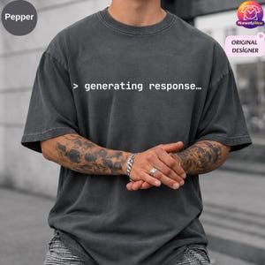 May include: A charcoal gray short-sleeve t-shirt with a crew neckline. The front of the shirt features the white text "> generating response..." printed in a monospaced font. The fabric has a washed, vintage-style appearance.